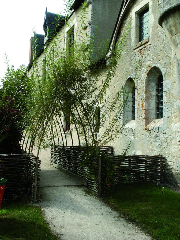 Passage bordé d'osier devant une maison en pierre